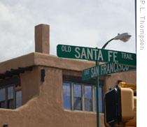 A modern sign marks the Santa Fe Trail. Behind, an example of adobe architecture