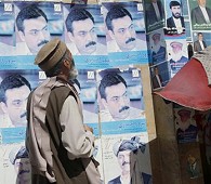 An Afghan man reads written slogans of a provincial candidate as portraits of presidential candidates are seen on posters pasted on a wall in Kabul, 2 Aug 2009